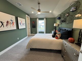Model Home A sports-themed bedroom with green walls, vibrant artwork, a cozy bed, and decorative baskets holding balls.