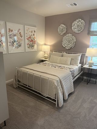 A cozy bedroom featuring floral wall art, a soft carpet, and elegant lighting, creating a serene and inviting atmosphere.
