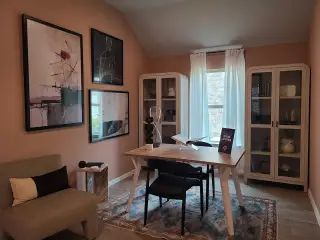 A cozy home office with modern art, bookshelves, a wooden desk, and natural light illuminating the space.