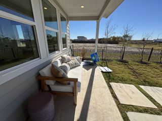 Model Home A cozy patio with a cushioned bench and pillows, bathed in sunlight, opens to a fenced yard and scenic views.