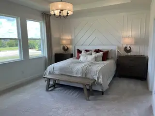 Model Home A bright bedroom featuring a chevron accent wall, cozy bedding, elegant lighting, and large windows with scenic views.