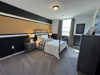 A cozy bedroom with a stylish accent wall, modern lighting, and plush carpeting.