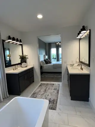 A modern bathroom with dual vanities, sleek black light fixtures, and a spacious tub leading into a cozy bedroom.