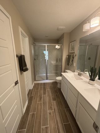 A modern bathroom with wood-look tile flooring, a glass shower, dual sinks, and stylish lighting.