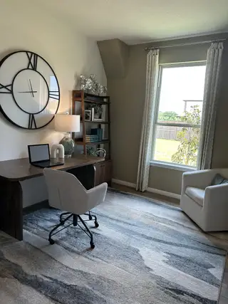 A modern home office with a sleek desk, cozy chair, and large decorative wall clock by the window.