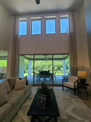 Model Home A spacious living room with tall windows, a cozy sofa, modern decor, and a view of the lush patio and garden.