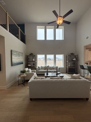 A spacious living room with high ceilings, neutral-toned sofas, modern art, and ample natural light through large windows.