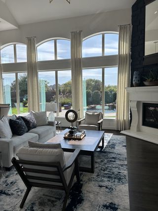 A bright living room with large arched windows, elegant seating, and a cozy fireplace, overlooking a lush garden.