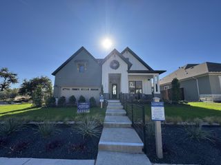 Model Home A bright and inviting home with a covered porch, elegant landscaping, and a welcoming pathway in Headwaters by David Weekley Homes.