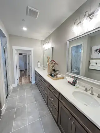 A modern bathroom with a double vanity, sleek counters, elegant lighting, and tiled flooring.