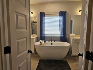A spacious bathroom with a freestanding tub, dual vanities, and modern lighting in Kingston by DRB Homes (Locust Grove, GA).