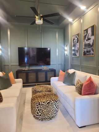 Model Home A chic living room with paneled walls, plush sofas, leopard print accents, and a sleek ceiling fan.
