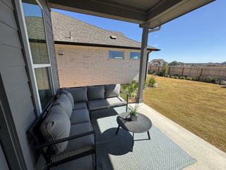 A cozy outdoor patio with gray seating, a round coffee table, and a view of a well-kept lawn.