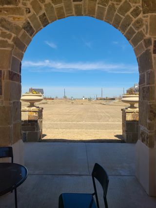 A charming stone archway overlooks a bright, open landscape in Village on Main Street by CB JENI Homes (Frisco, TX).