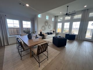 A spacious, sunlit living and dining area with sleek furniture, wood flooring, and large windows creating an open, airy feel.