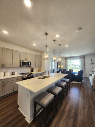 Model Home A modern kitchen with sleek cabinetry, a spacious island, and elegant lighting, opening to a cozy dining area.