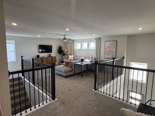 Model Home An elegant loft space with cozy seating, a sleek TV setup, and modern railings, bathed in natural light.