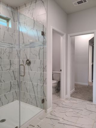 A modern bathroom featuring marble-patterned tiles, a sleek glass shower, and bright natural lighting.