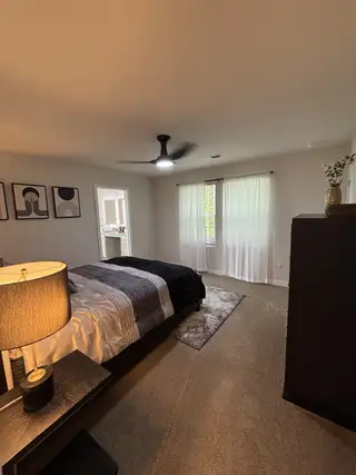 Model Home A cozy bedroom featuring soft carpet, a sleek ceiling fan, and modern artwork for a stylish and inviting atmosphere.
