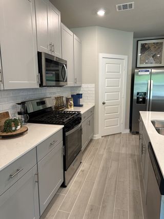 Model Home A modern kitchen featuring sleek gray cabinets, stainless steel appliances, and elegant wood-look tile flooring.