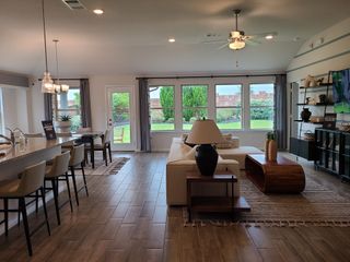 An inviting open-plan living area with large windows, modern furnishings, and hardwood floors, overlooking a lush backyard.