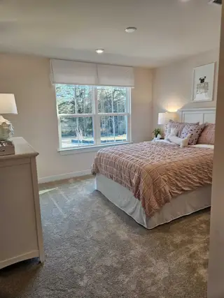 A cozy bedroom with a plush carpet, soft bedding, and a large window offering scenic forest views.