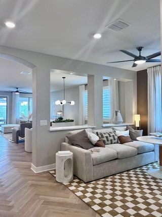 A cozy living room featuring a plush sectional sofa, modern ceiling fan, and elegant lighting, with open spaces and patterned rug.