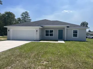 Street view A modern white home with a spacious garage and lush lawn in Marion Oaks by Zephyr Homes (Ocala, FL).