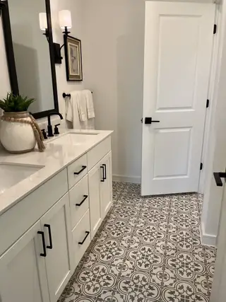A chic bathroom with patterned tile flooring, a sleek white vanity, black hardware, and elegant lighting.