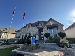 Street view A stunning home with manicured landscaping and flag displays in Parkside On The River by Highland Homes (Georgetown, TX).