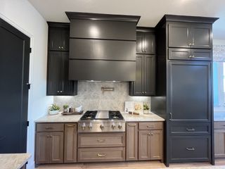 Model Home A sophisticated kitchen with black upper cabinets, warm wood lower cabinets, and a striking range hood design.