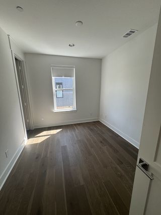 Model Home A bright room with sleek wooden floors and a single window, offering a blank canvas for personalization.