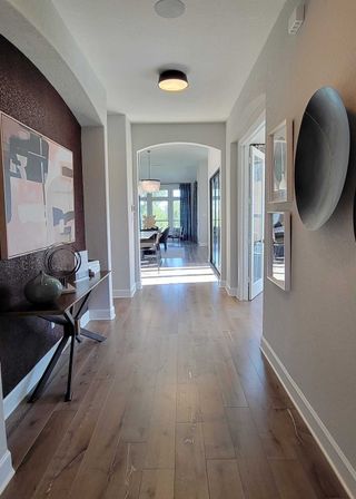 A bright hallway with wood flooring, abstract art, and modern decor leading to a sunlit dining area.