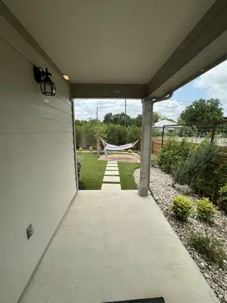 A cozy covered patio with a walkway leading to a hammock and a lush garden view.