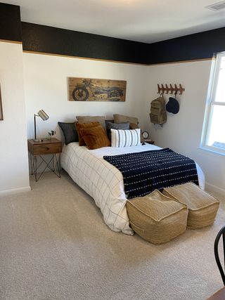 A bedroom with a dark accent stripe, a patterned throw on the bed, woven ottomans, and a motorcycle-themed artwork on the wall.