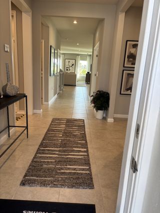 Contemporary hallway with tile floors, a patterned rug, and framed artwork leading to a bright living area.