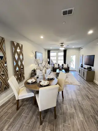 Model Home A cozy dining and living area with elegant decor, featuring a stylish round table, cream chairs, and wood tile flooring.