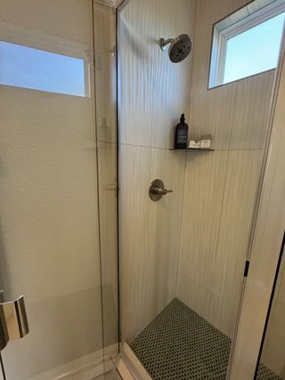 Model Home A modern shower with sleek glass doors, textured tiles, and a small window for natural light.