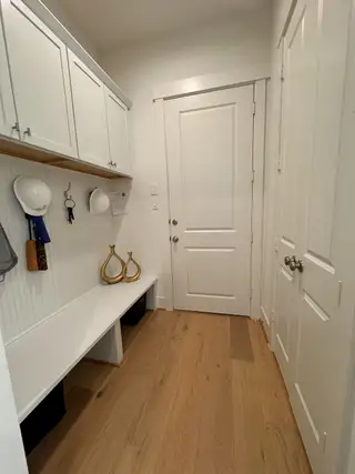 Model Home A functional mudroom with white cabinets, wood flooring, and cozy bench seating for organization and storage.
