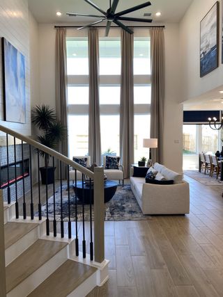 A spacious living area with high ceilings, large windows, a modern fan, and a cozy seating arrangement.