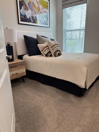 Model Home Cozy bedroom with plush carpet, modern decor, and soft lighting, featuring a neatly dressed queen bed and stylish artwork.