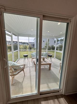 A cozy sunroom with wicker seating, a wooden table, and large sliding glass doors opening to a lush backyard.