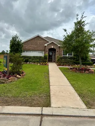Street view A charming brick home with a lush yard and pathway in Freeman Ranch by LGI Homes (Katy, TX).