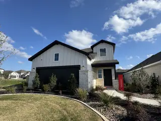Street view A modern white home with dark accents and landscaping in Garten Haus Cottages At Solms Landing by Wes Peoples Homes (New Braunfels, TX).