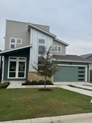 Street view A modern multi-level gray home with sleek lines and landscaped yard in Whisper Valley by Thurman Homes (Manor, TX).