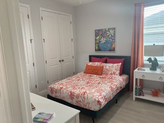A vibrant bedroom with coral-themed bedding, bright pillows, a colorful painting, and a white nightstand with decorative accents.
