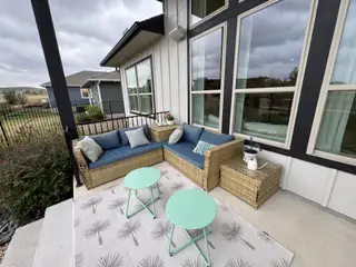A cozy patio featuring a wicker sofa, blue cushions, and mint coffee tables on a patterned rug.