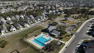 Charming neighborhood aerial with landscaped streets and a community pool in 6 Creeks by New Home Co. (Kyle, TX).