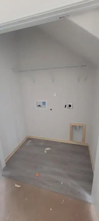 A utility closet with sleek gray flooring, wiring connections, and ample shelving space. Ideal for washer and dryer setup.