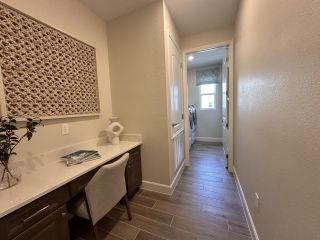 Model Home A cozy hallway with a stylish desk setup, textured wall art, and tiled flooring leading to a bright laundry room.